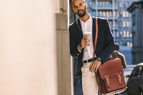 Businessman leaning to wall outdoors with coffee