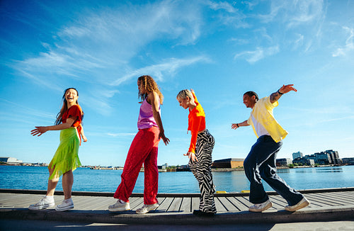 Friends walk playfully in line along the waterfront on a sunny day