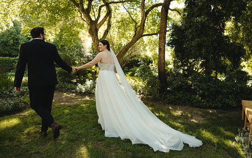 Bride and groom walking hand in hand in sunlit garden setting