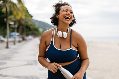 Fit and happy: Woman laughing while standing on the beach in fitness wear