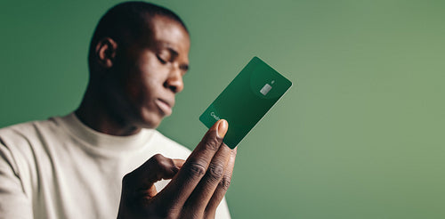 Paying with credit currency: Young black man holding a green credit card in a studio