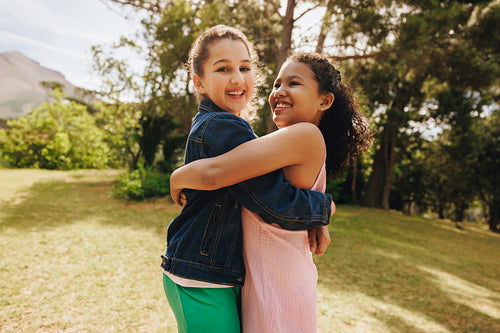Two smiling friends hugging outdoors in a sunny park setting