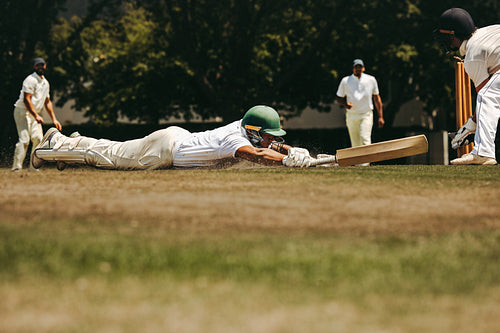 Male cricket player diving to save his wicket during a match