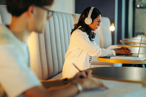 Students studying for exams in a modern shared workspace. Focused individuals using technology and taking notes, creating a productive study environment.