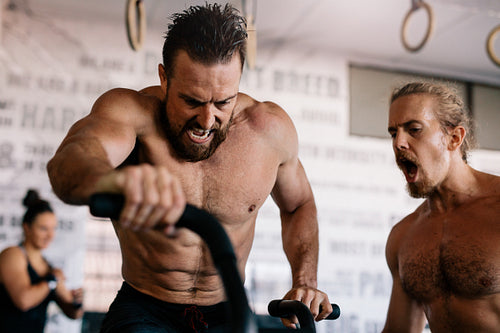Muscular man riding on exercise bike with personal trainer