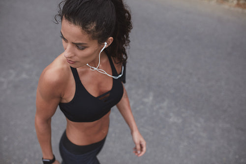 Muscular young female athlete with earphones outdoors