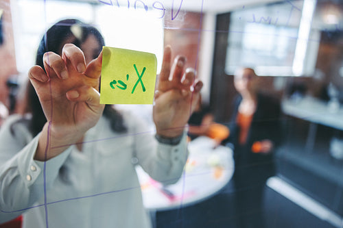 Young businesswoman sticking adhesive notes to a glass wall