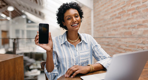 Happy small business owner showing a smartphone in a warehouse