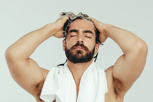 Young man massaging his scalp as he applies shampoo to his hair