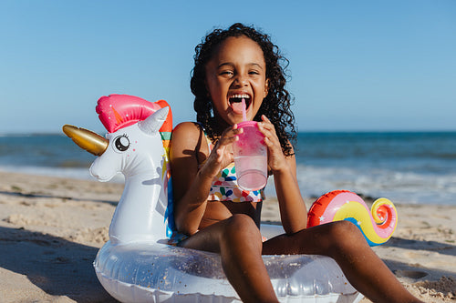 Joyful child enjoying summer vacation at the beach with inflatable unicorn