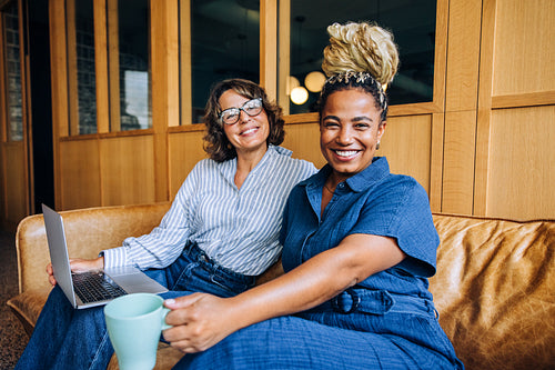Two women smiling together on a couch in a modern interior space