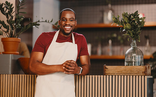 Successful entrepreneur smiling in cafe environment, wearing an apron and standing at the counter