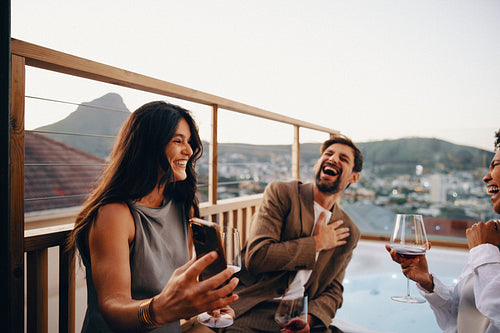 Friends enjoying wine and laughter on a scenic rooftop balcony at sunset