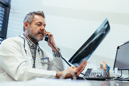 Doctor checking x-ray and talking on telephone at clinic