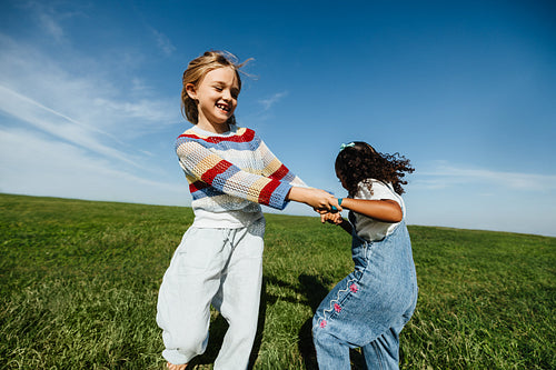 Two girls spinning and playing in a grassy field
