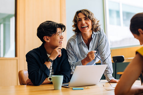 Professionals engaged in lively discussion around a laptop during a meeting