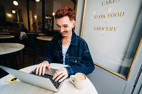 Young man working on laptop in bright cafe