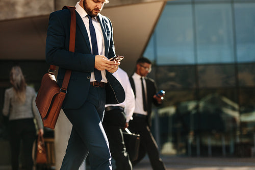 Business people using mobile phone while walking on street to office