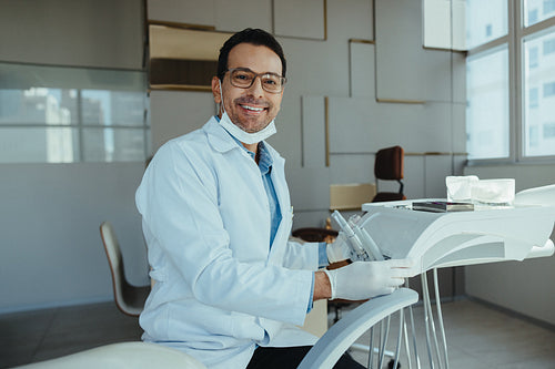 Male dentist seated near chair in clean clinic portrait