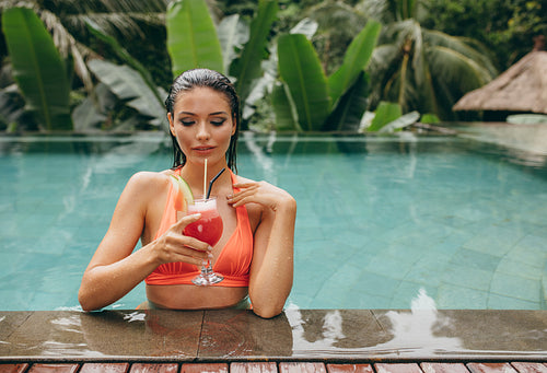 Young woman relaxing in pool and having cocktail