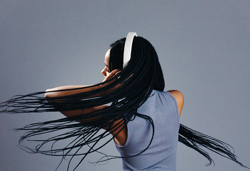 Young woman flipping her braids while listening to music on headphones