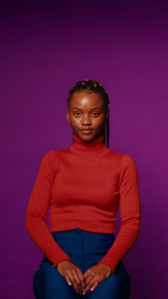 Young woman sits calmly against a vibrant purple background looking directly at the camera