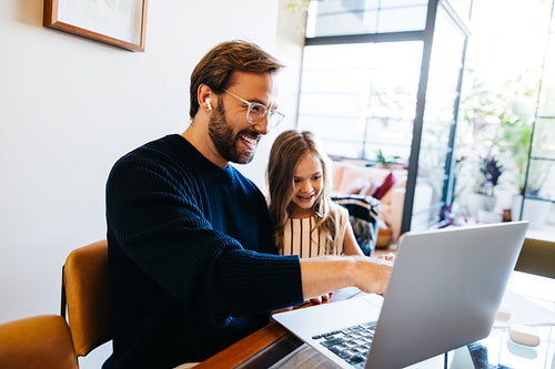 Father and daughter smiling while using laptop at home
