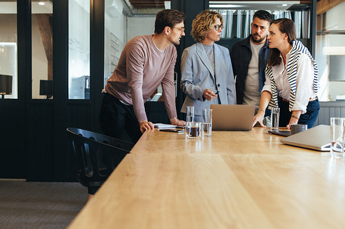Design team discussing a project in a meeting, they're standing together around a laptop in a boardroom