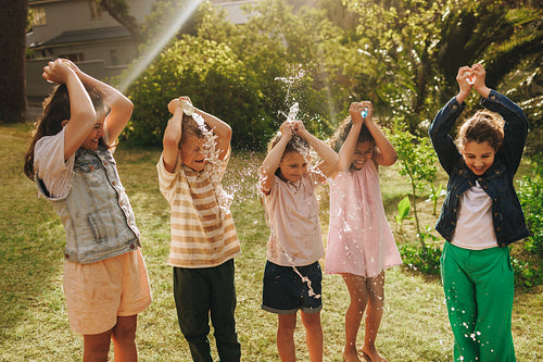 Five children enjoying a fun water splash activity on a sunny day outdoors