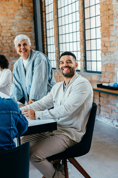 Diverse age range of colleagues engaged in a friendly meeting in a bright, modern office with exposed brick and large windows