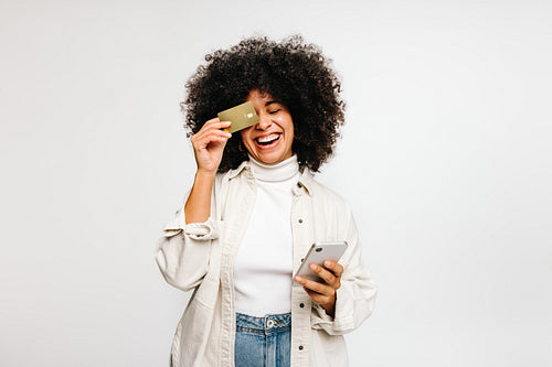 Happy young woman holding a credit card and a smartphone