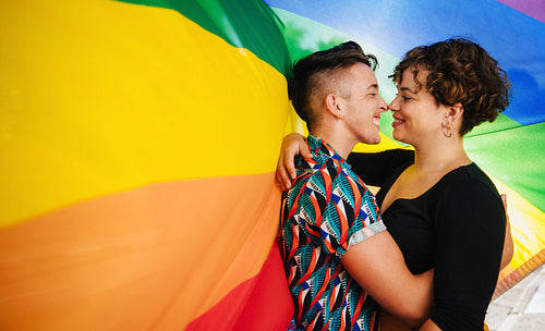 Affectionate queer lovers bonding against a rainbow flag
