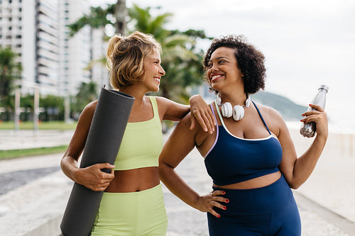 Two friends enjoying a beach workout with yoga mat and water bottle
