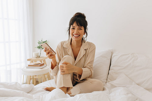 Smiling woman sitting on bed holding mobile phone