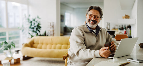 Senior man uses a laptop with coffee at home