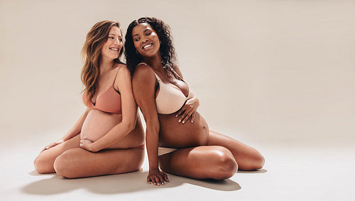 Expecting moms smiling and sitting together in a pregnancy photoshoot