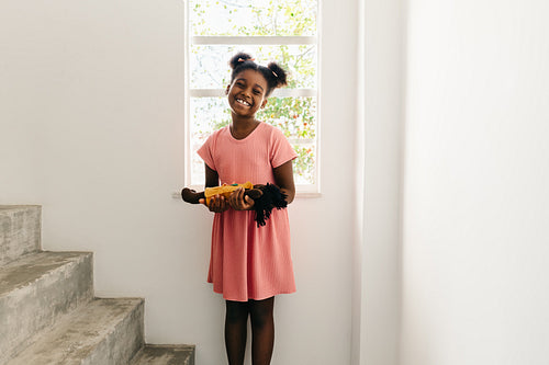 Happy afro-haired girl holding her doll at home