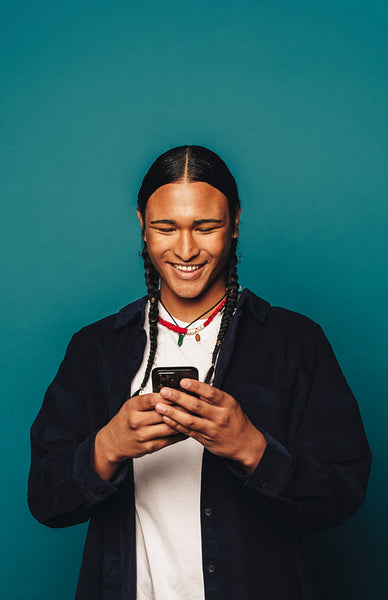 Happy young man checking phone in a blue studio, wearing casual clothing