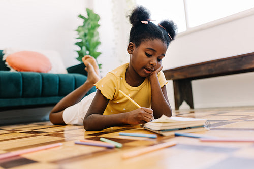 Little girl engaged in educational activity with colour pencils and a colouring book at home