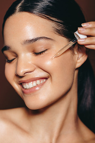 Happy young woman using a beauty serum on her face