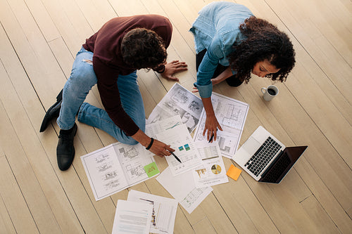 Business colleagues sitting on the floor and discussing work with business papers spread on the floor