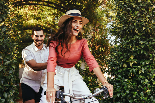 Playful young man pushing his girlfriend on a bike
