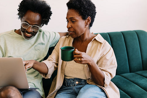 Mature couple chatting and using laptop together on a couch