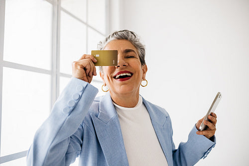 Online and mobile banking at work: Happy senior business woman holding a credit card and a smartphone