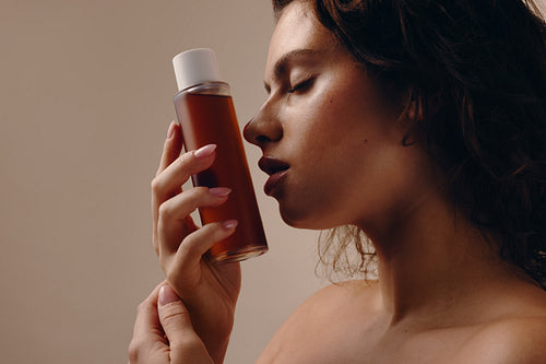 Woman smelling skincare bottle in serene beauty portrait