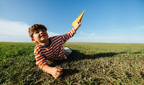 Young boy playing with paper airplane outdoors inspired by imagination and creativity