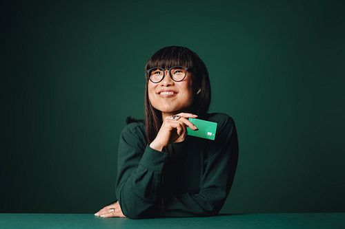 Confident woman holding credit card in studio portrait on green background