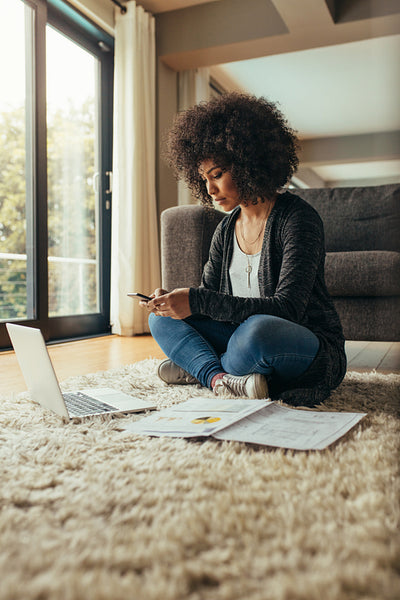 Female using mobile with laptop and documents on floor at home