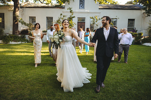 Newlywed couple walking joyfully with guests in a garden wedding setting