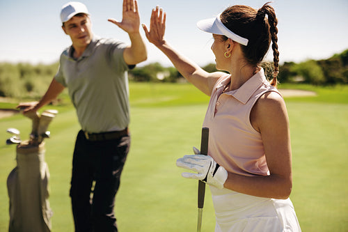 Sportsman and sportswoman sharing a high five on the golf course wearing golfing attire